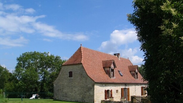 Ein Steinhaus mit rotem Ziegeldach, einer kleinen Veranda und einem eingezäunten Garten.