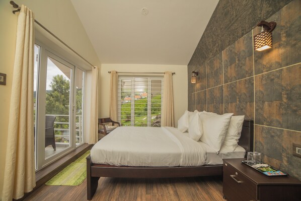 A bedroom with a large bed, a nightstand, and a view of greenery through the window. - CozyVillas (Ootacamund)
