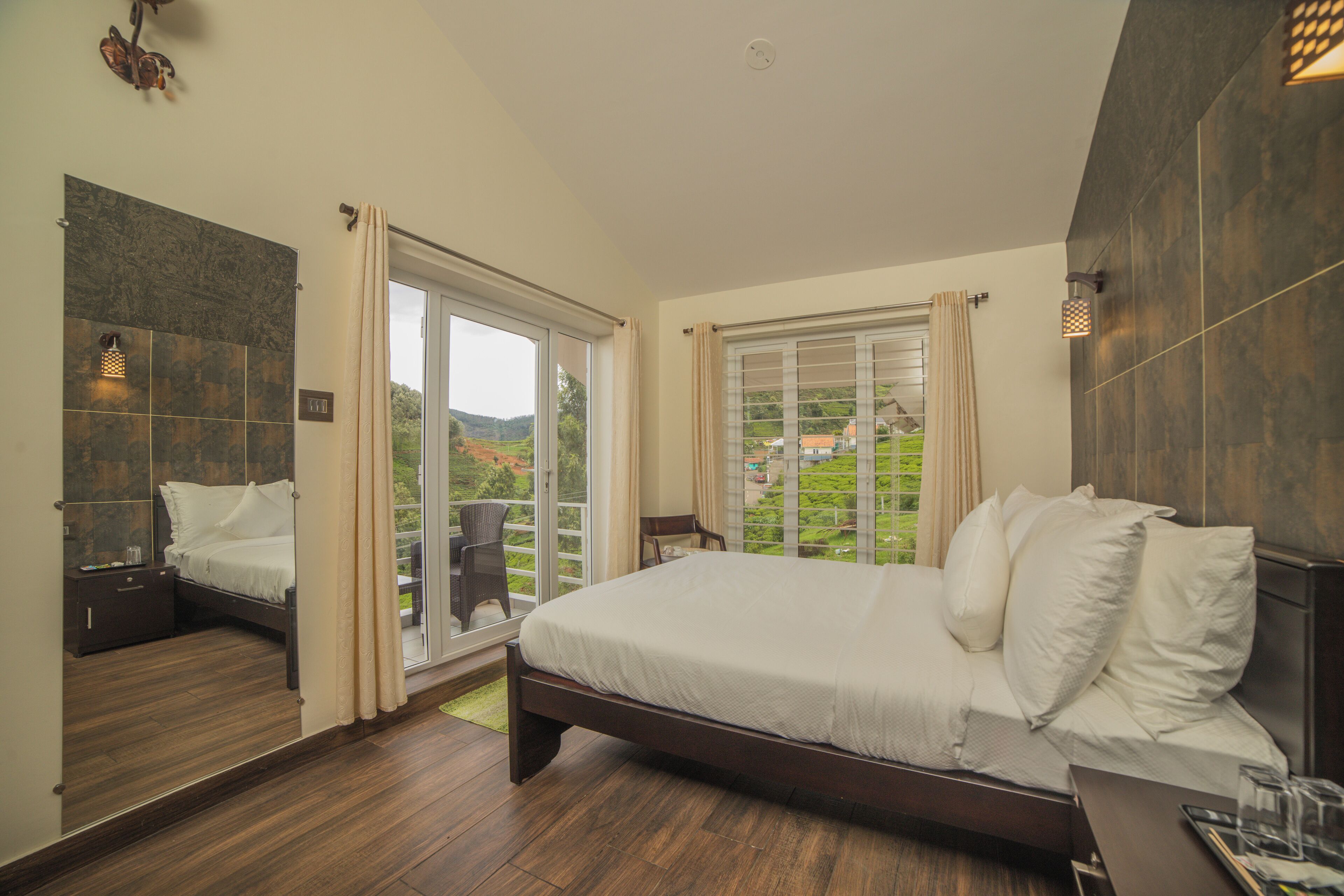 A modern bedroom with a large bed, a separate seating area, and a balcony with a view of the countryside.