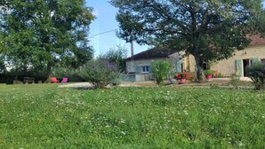 Uma casa de pedra rústica com um jardim da frente, rodeada por árvores e um céu limpo.
