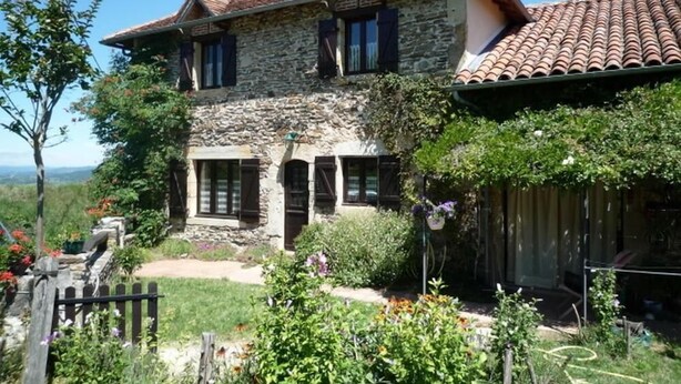 A two-story stone house with a tiled roof, surrounded by lush greenery and a wooden fence. - Gîtes de France® - Gîte in Negral (SAINT-VINCENT-DU-PENDIT)