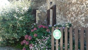 A stone building with a wooden fence, a sign indicating a city of France, and a variety of flowering plants. - Gîtes de France® - Gîte in Negral (SAINT-VINCENT-DU-PENDIT)