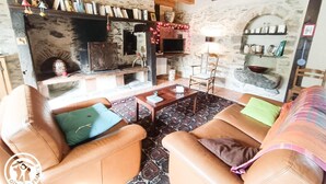 A cozy living room with leather sofas, a fireplace, bookshelves, and a stone wall. - Gîtes de France® - Gîte in Negral (SAINT-VINCENT-DU-PENDIT)