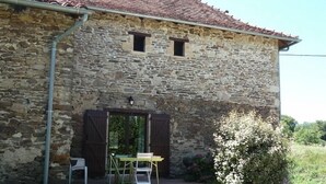 A stone building with a tiled roof, two small windows, a door with shutters, and a table with chairs outside. - Gîtes de France® - Gîte in Negral (SAINT-VINCENT-DU-PENDIT)