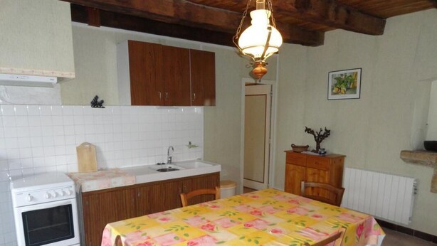 A kitchen with a wooden table, chairs, a stove, and a sink. - Gîtes de France® - Chez Simon (SAINT-VINCENT-RIVE-D'OLT)
