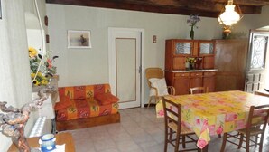 A cozy living room with a sofa, a dining table with chairs, a wooden cabinet, and a chandelier. - Gîtes de France® - Chez Simon (SAINT-VINCENT-RIVE-D'OLT)
