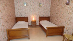 A bedroom with two wooden beds, a small bedside table with a lamp, and a chair. - Gîtes de France® - Chez Simon (SAINT-VINCENT-RIVE-D'OLT)