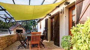 An outdoor patio with stone flooring, wooden furniture, and a yellow canopy. - Gîtes de France® - Le Gîte des Buis du Causse (SAINT SULPICE)