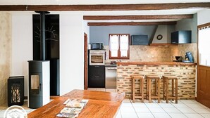 A cozy kitchen with a wooden table, a stove, and a brick wall. - Gîtes de France® - Le Gîte des Buis du Causse (SAINT SULPICE)