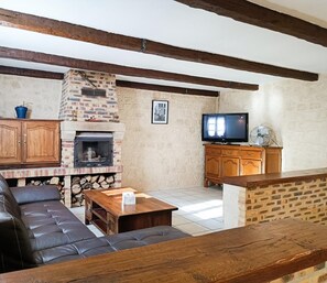 Un salon chaleureux avec une cheminée en pierre, des poutres apparentes, un canapé en cuir et un téléviseur.