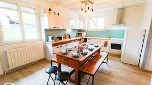 A modern kitchen with wooden cabinets, a dining table set for four, and a built-in oven. - Gîtes de France® - La Vue Ombragée (VIAZAC)