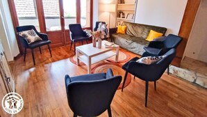 A living room with a sofa, two armchairs, a coffee table, and a bookshelf. - Gîtes de France® - La Vue Ombragée (VIAZAC)