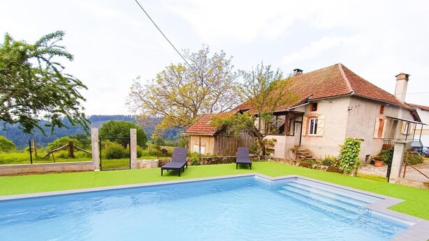 A swimming pool with two lounge chairs, surrounded by a well-maintained lawn and a house with a red-tiled roof. - Gîtes de France® - La Vue Ombragée (VIAZAC)