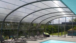 Una piscina techada con sillas de descanso y un cerramiento de vidrio.