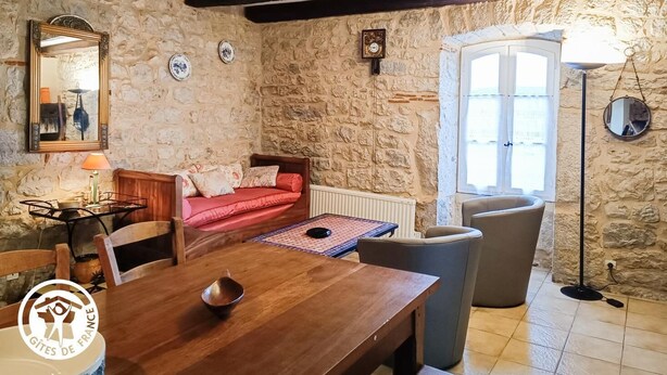 Una habitación rústica con paredes de piedra, una mesa de madera para comer, un sofá rojo y un ventanal grande.