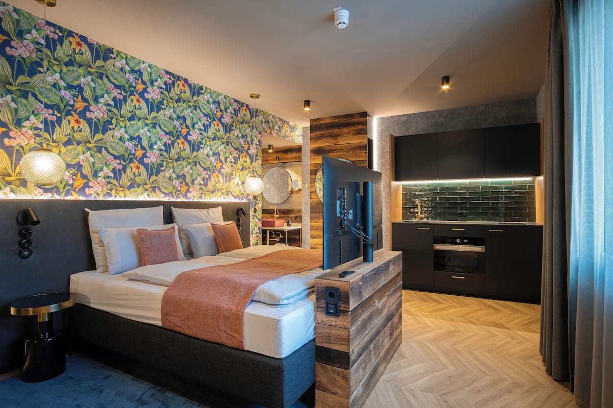 A modern bedroom with a large bed, a TV, and a kitchenette.