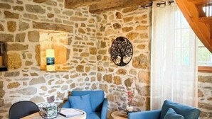 Un interior rústico con paredes de piedra, vigas de madera, una mesa con sillas y una lámpara colgante.