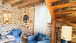 Un interior rústico con paredes de piedra, techo de madera, un sof á azul, una mesita y una lámpara.
