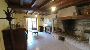 Uma sala de estar ampla com lareira de pedra, vigas de madeira, uma mesa de jantar e uma televisão.