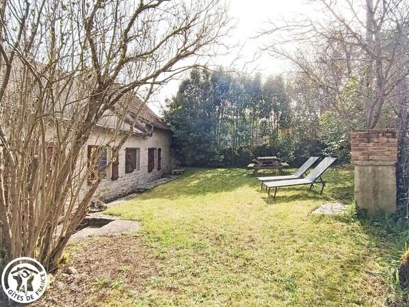 A rustic stone house with a thatched roof, a grassy yard, and two sun loungers.