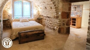 Ein rustikales Schlafzimmer mit Steinwänden, einem Bett, einem Fenster und einem Holzkabinett.