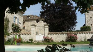 Ein Steinhaus mit Schwimmbecken, umgeben von üppigem Grün und blühenden Pflanzen.