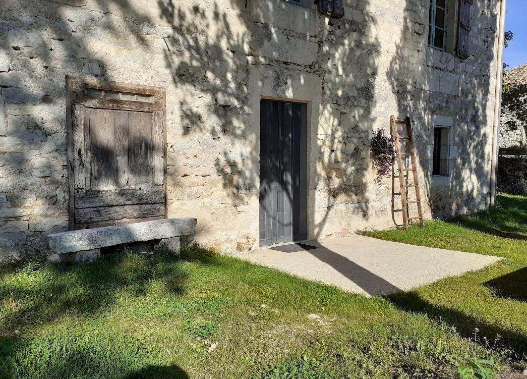 Edifici de pedra rústic amb porta i finestra de fusta, un camí de formigó i una banca de fusta.
