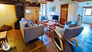 A cozy living room with a sofa, chairs, a TV, and a wooden coffee table. - Gîtes de France® - GITE LA BUISSIERE (GREALOU)