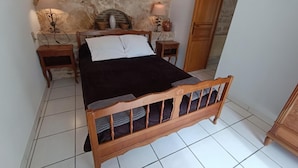 Quarto com cama de madeira, duas mesas de cabeceira, parede de pedra e guarda-roupa de madeira.