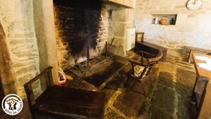 Un rustico camino in pietra con canna fumaria, una panca in legno e un piccolo ripiano con ceramiche.