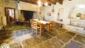 Una stanza rustica con pavimento in pietra, un tavolo e sedie di legno, un camino e pareti in pietra.