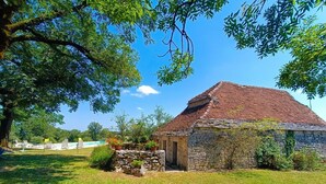 Un edificio in pietra con tetto in tegole rosse, immerso nel verde di erba e alberi.