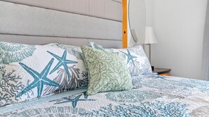 Un lit avec une couvre-lit à motifs, deux oreillers ornés de motifs en forme d’étoile de mer et de feuilles, une lampe de chevet et une tête de lit en bois.