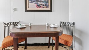 Une table à manger avec deux chaises, un tableau encadré au-dessus, et une petite lampe de table.