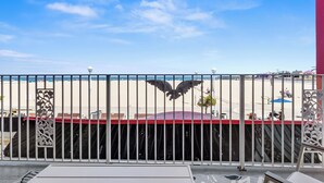 Une vue à travers une clôture en métal ornée d’un emblème représentant un aigle, donnant sur une plage et un bâtiment avec un toit rouge.