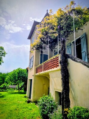 A two-story building with a balcony, surrounded by greenery.