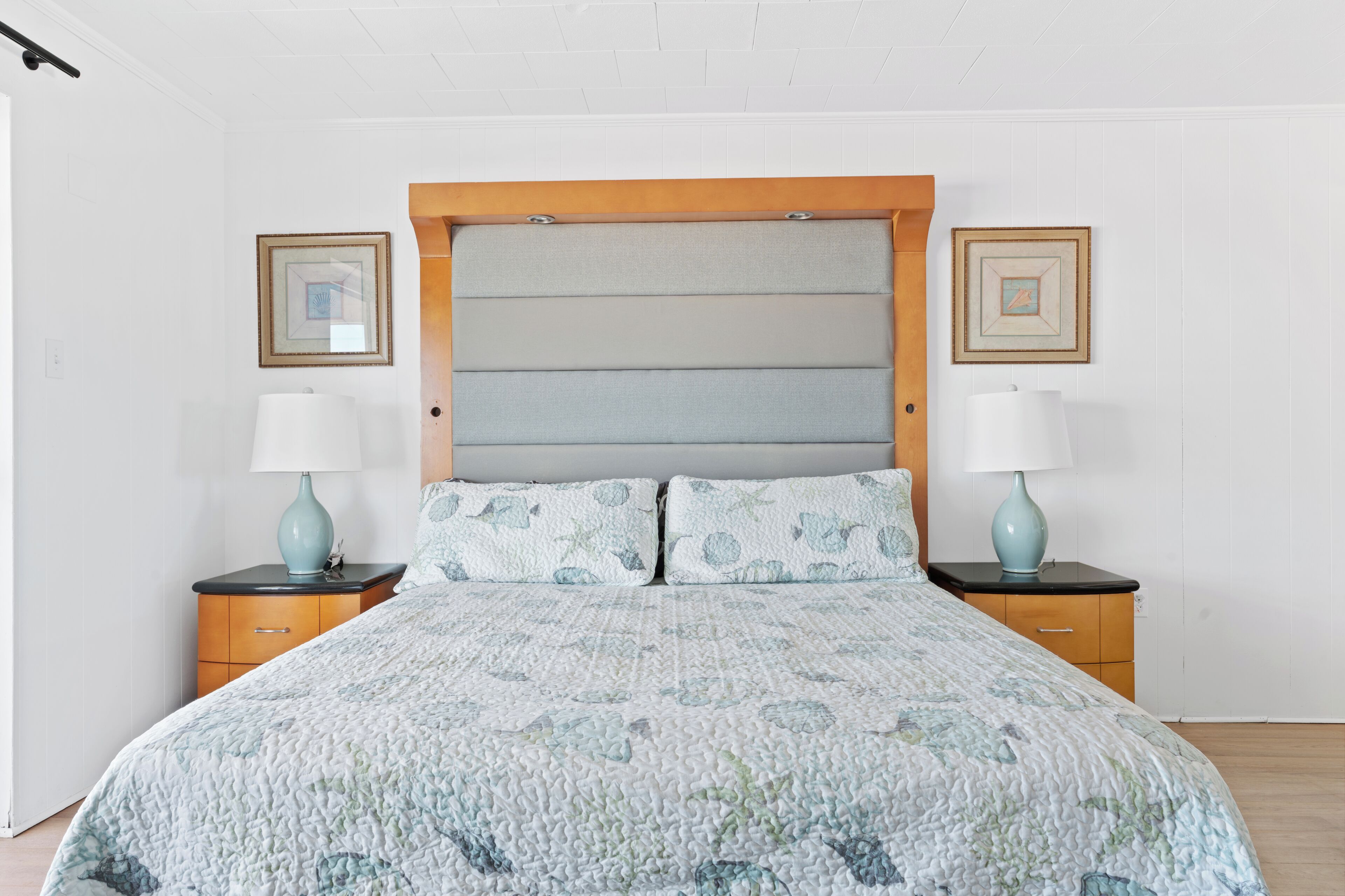 A bed with a quilted headboard, two bedside tables with lamps, and framed pictures on the wall.