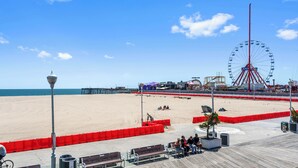 A beach with a Ferris wheel, a pier, and a boardwalk with benches.