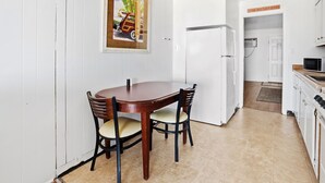 A dining area with a wooden table and chairs, a white door leading to a kitchen, and a wall-mounted picture.