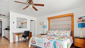 A bedroom with a bed, a desk, a chair, a nightstand, and a ceiling fan.