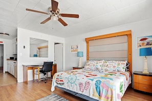 Une chambre à coucher comprenant un lit, un bureau, une chaise, une table de chevet et un ventilateur de plafond.