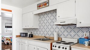 A kitchen with white cabinets, a microwave, a stove, and patterned backsplash.