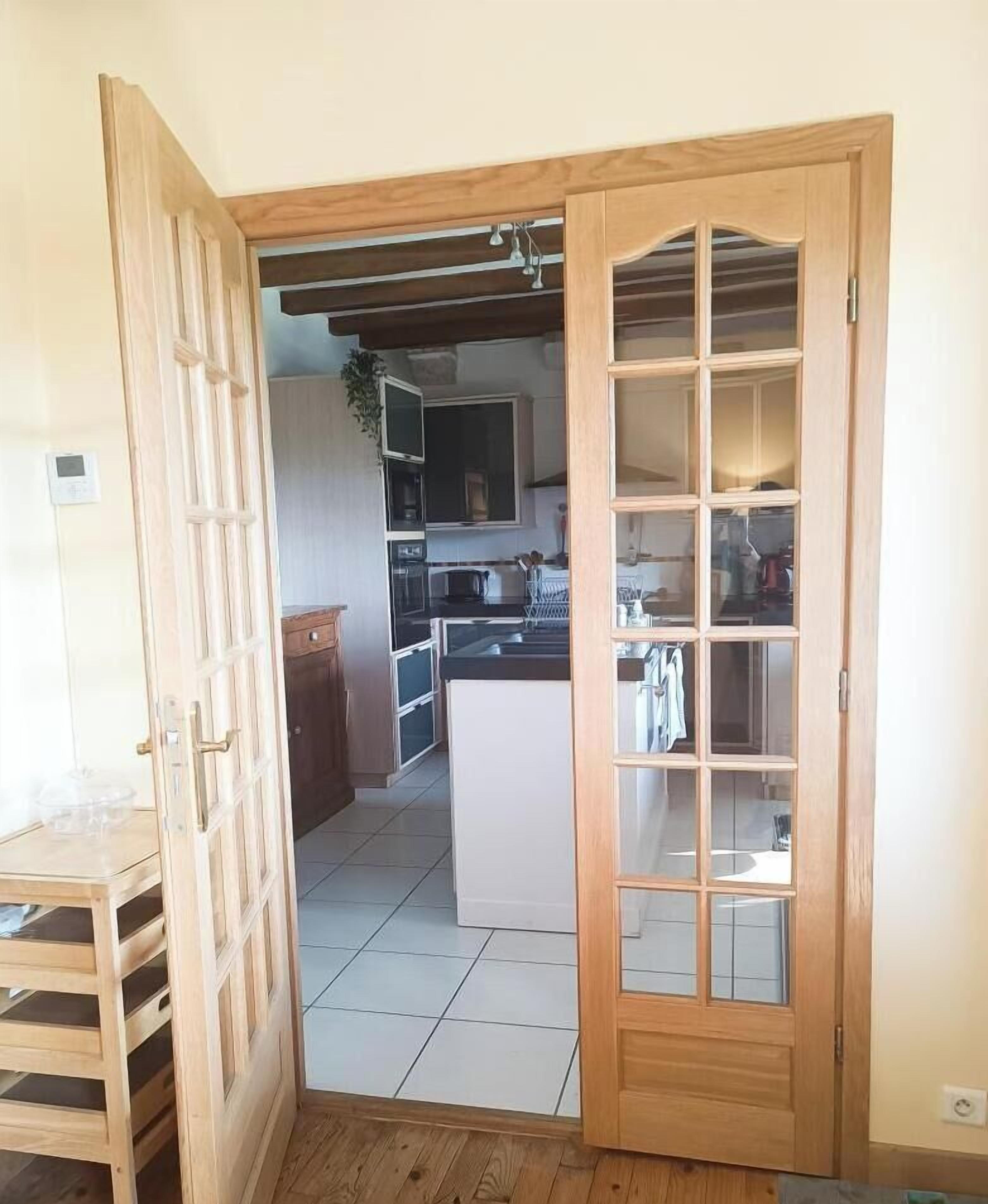 A wooden door leading to a kitchen with a tiled floor, a refrigerator, and a countertop.