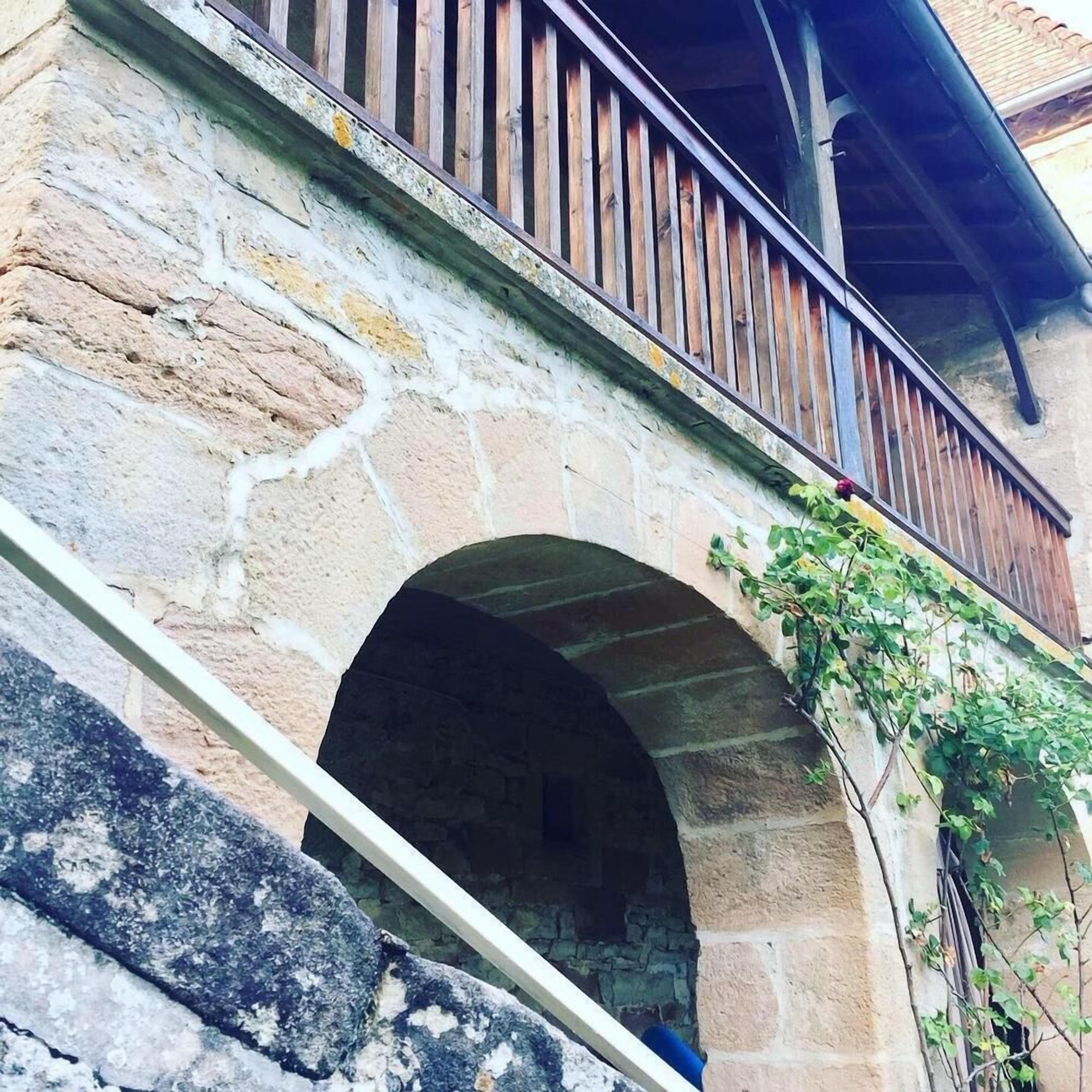 Un bâtiment en pierre doté d’un balcon en bois et d’une entrée en arc de cercle.