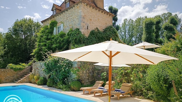 Uma casa de pedra com piscina, rodeada por vegetação exuberante e área de estar ao ar livre.