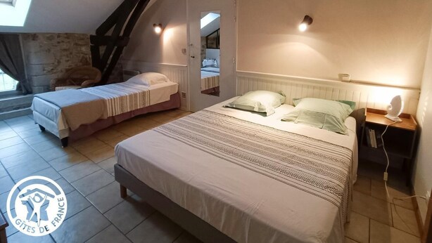 A bedroom with two beds, a stone wall, a sloped ceiling, and a small window. - Gîtes de France® - Gite de la Rivière Basse (MONTBRUN)