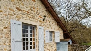 A stone building with white shutters, a tiled patio, and a metal railing. - Gîtes de France® - Gite de la Rivière Basse (MONTBRUN)