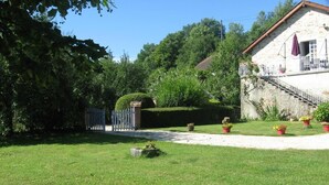 A stone building with a staircase leading to a balcony, surrounded by a well-maintained lawn and potted plants. - Gîtes de France® - Gite de la Rivière Basse (MONTBRUN)