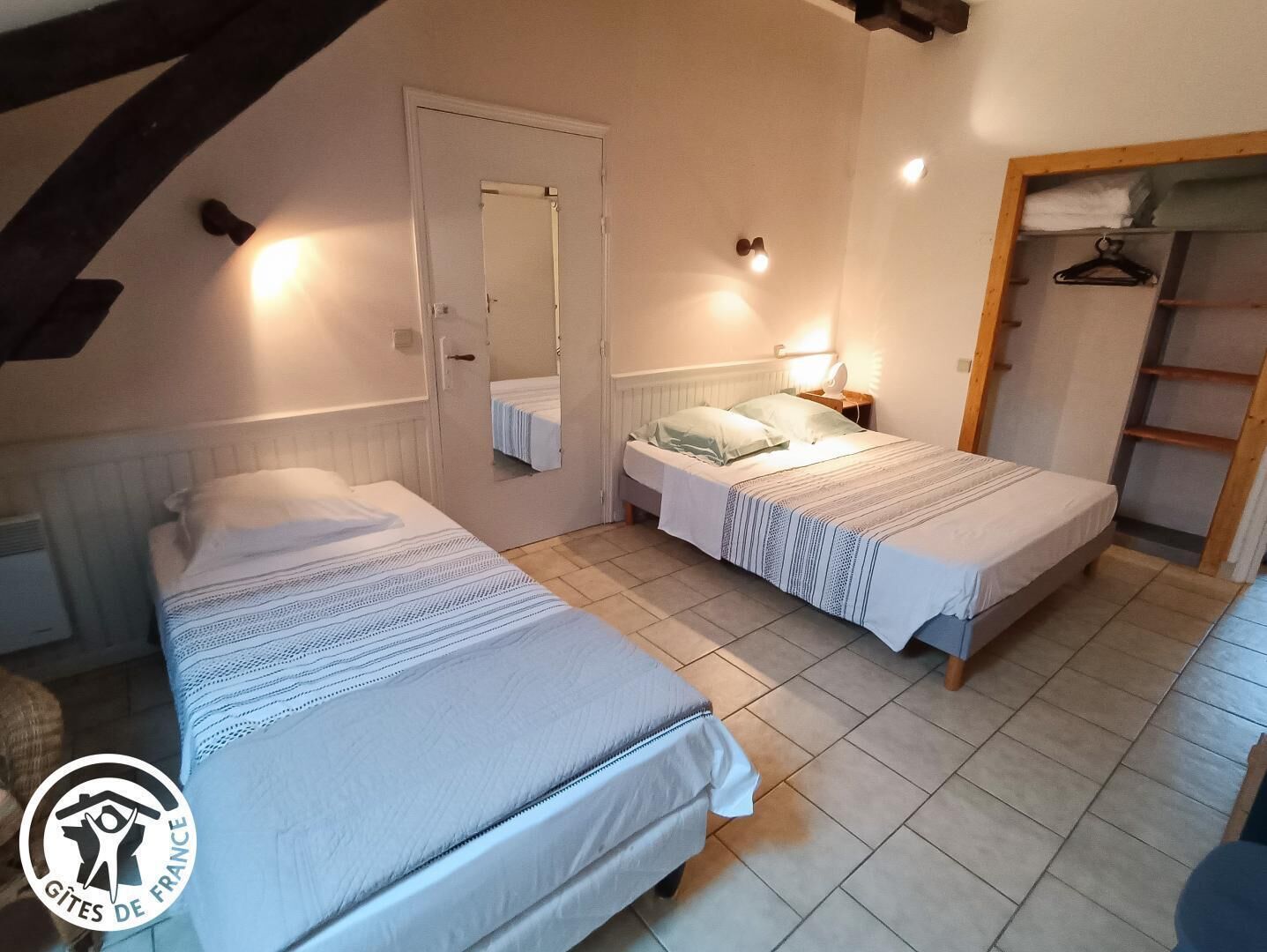 A bedroom with two beds, a wardrobe, a mirror, and a bedside lamp.