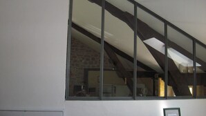 A room with a large window, exposed wooden beams, and a brick wall. - Gîtes de France® - Gite de la Rivière Basse (MONTBRUN)